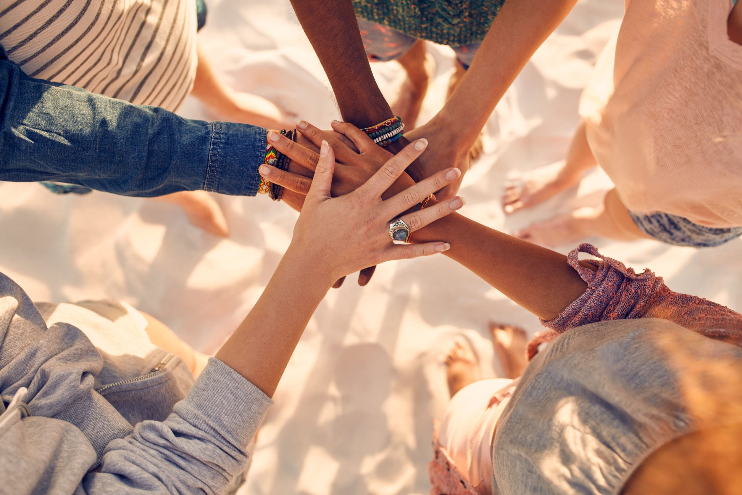 Closeup of group of mixed race friends on the beach with their hands stacked in the middle.