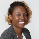 DrC Portrait of a woman with short, curly hair, smiling, and wearing a gray blazer over a white blouse