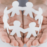 Hands holding a paper chain of human figures, symbolizing community, connection, and support.