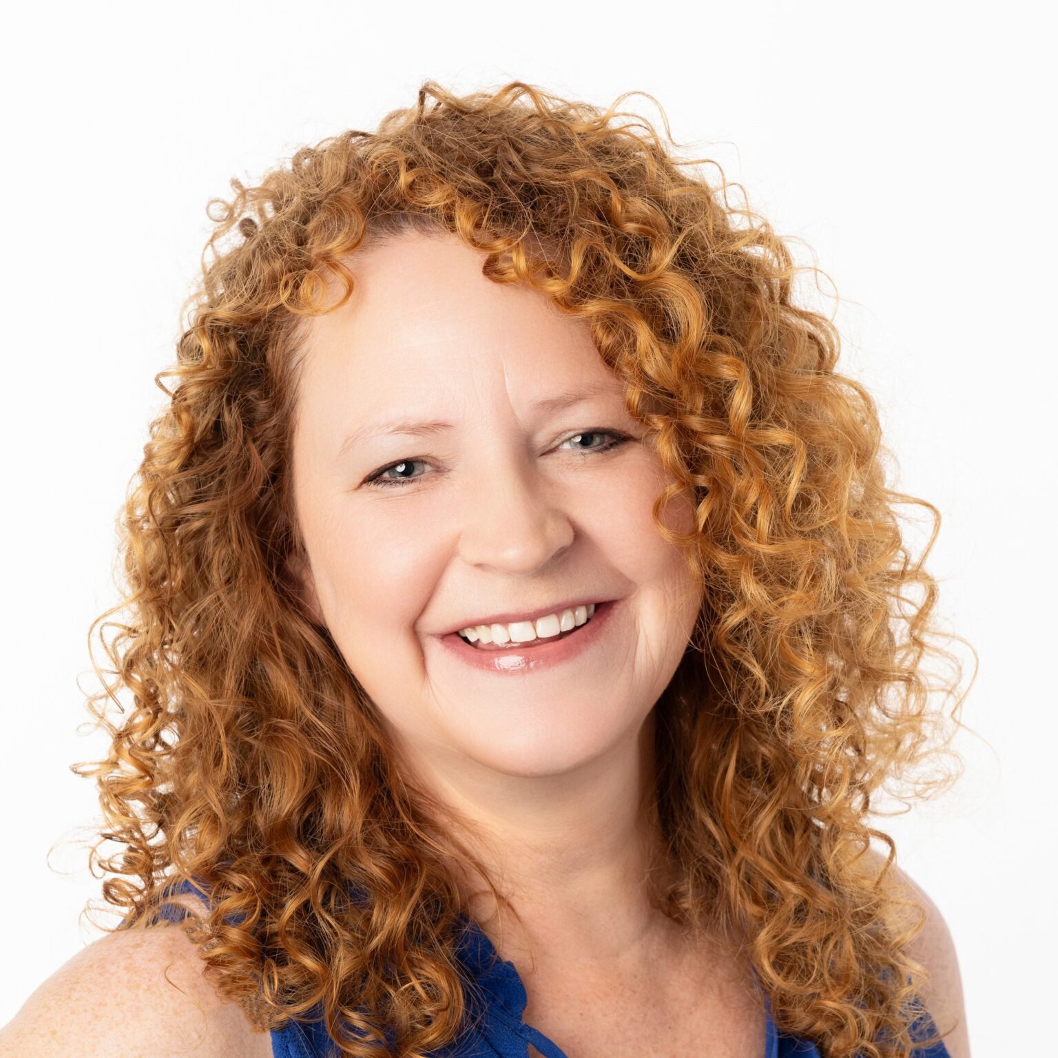 Carrie Pettus A woman with curly red hair smiles at the camera. She is wearing a sleeveless blue top.