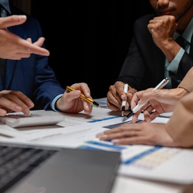 Close-up of professionals collaborating at a table with documents, charts, and a laptop.