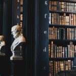 Cropped view of a row of dark bookshelves in a library, each adorned with a bust statue of a literary artist in front