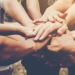 A close-up of multiple hands stacked on top of each other in a gesture of unity and teamwork.